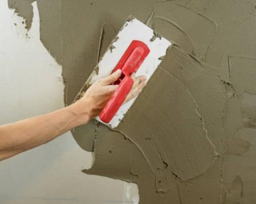 A worker plasters the wall with a spatula and applies a cement mix solution. The repairman lays the plaster on the drywall. Handyman repairs home. Laborer restore dwelling. Specialist covers up cracks
