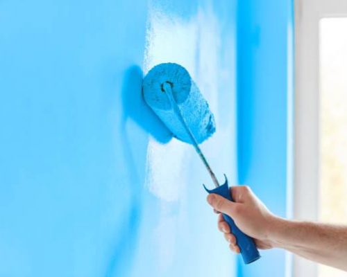 Male hand painting wall with paint roller. Painting apartment, renovating with blue color paint