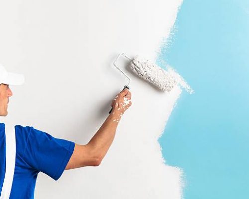 Back view of painter painting a wall with paint roller, with copy space