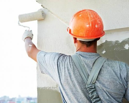 Young painting facade builder worker with roller at thermal insulation works