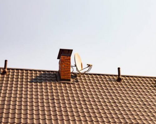 Satellite TV antenna near the chimney pipe on the roof of a house under a blue sky